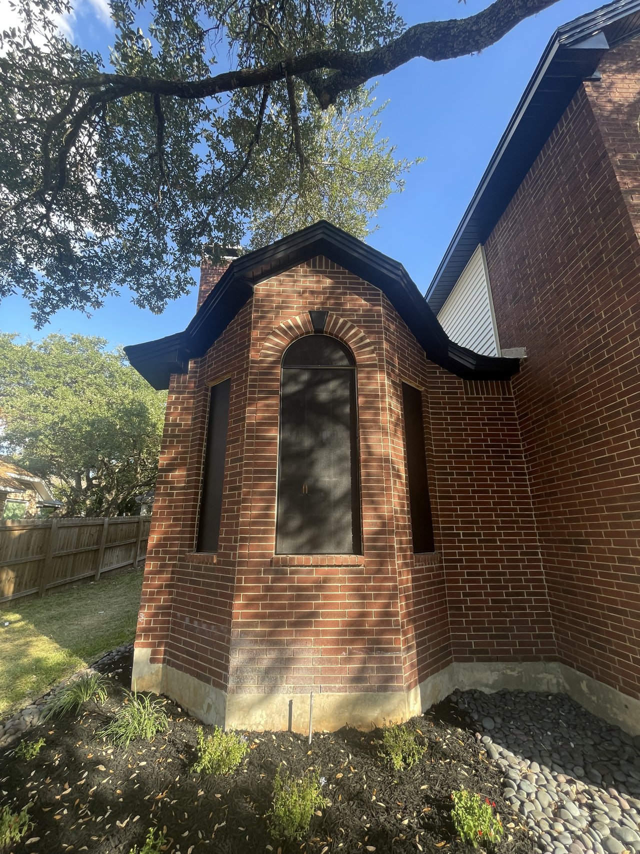 Custom-cut solar screen on arched turret window, red brick two-story home