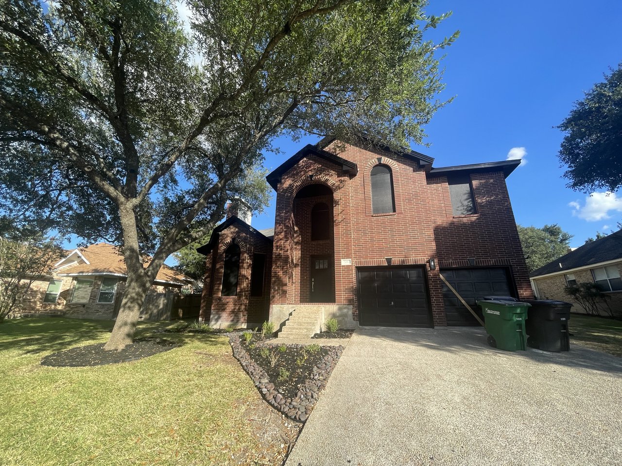 Two-story brick home with solar screens installed on all windows, tree-shaded front yard